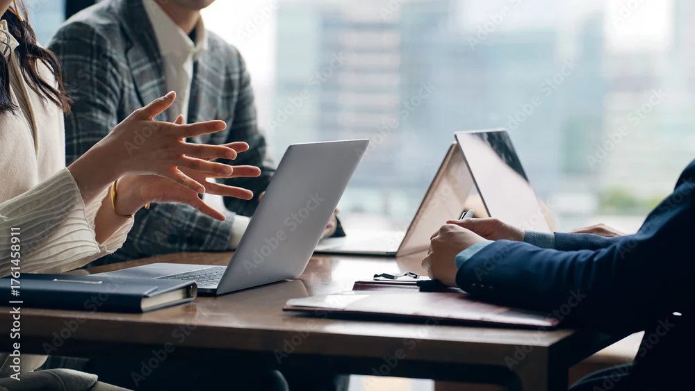 Mehrere Personen sitzen mit Laptops und Unterlagen an einem Tisch und diskutieren in einem Meeting.