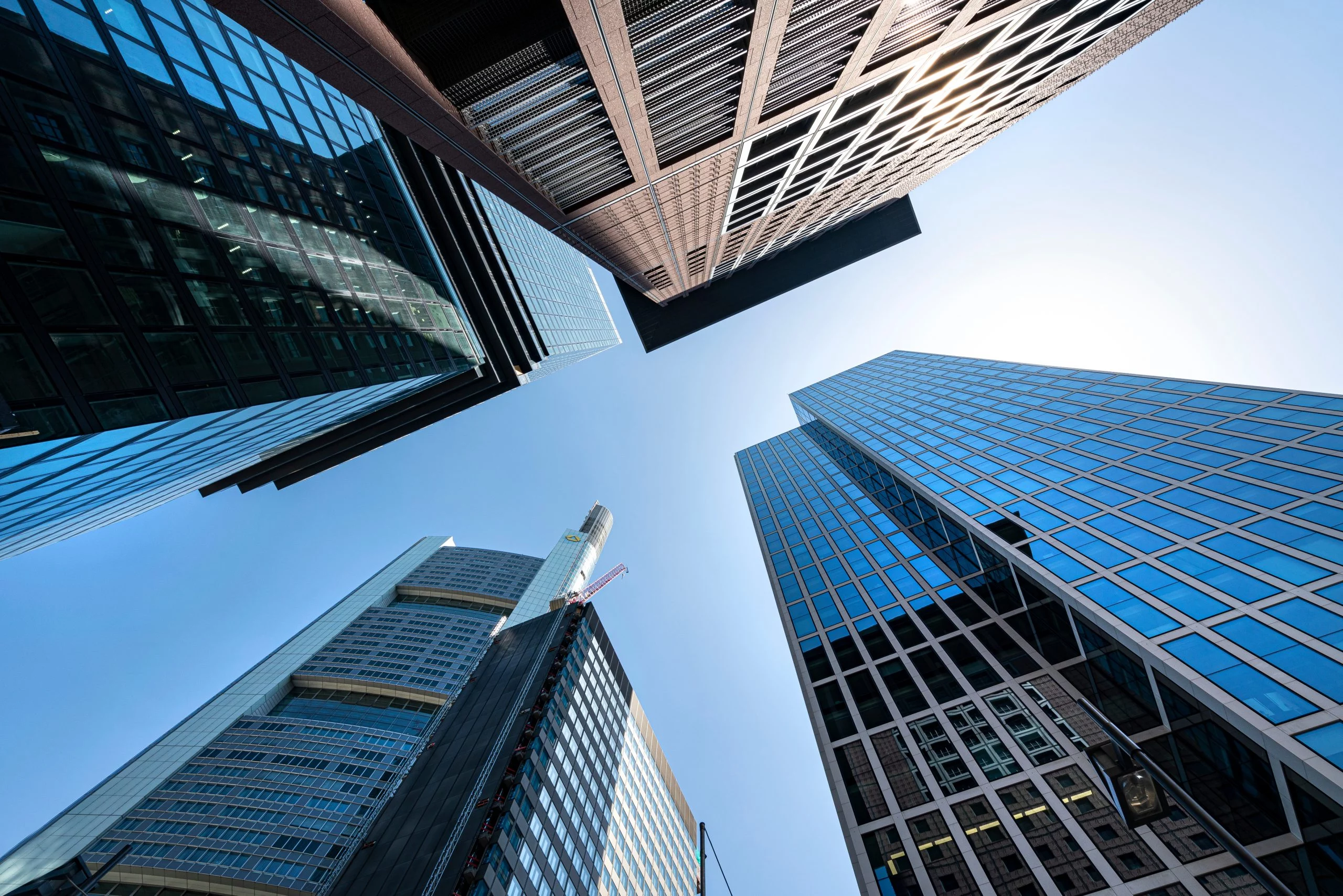 Blick von unten auf moderne Hochhäuser einer Finanzmetropole mit klarem Himmel und markanter Architektur.