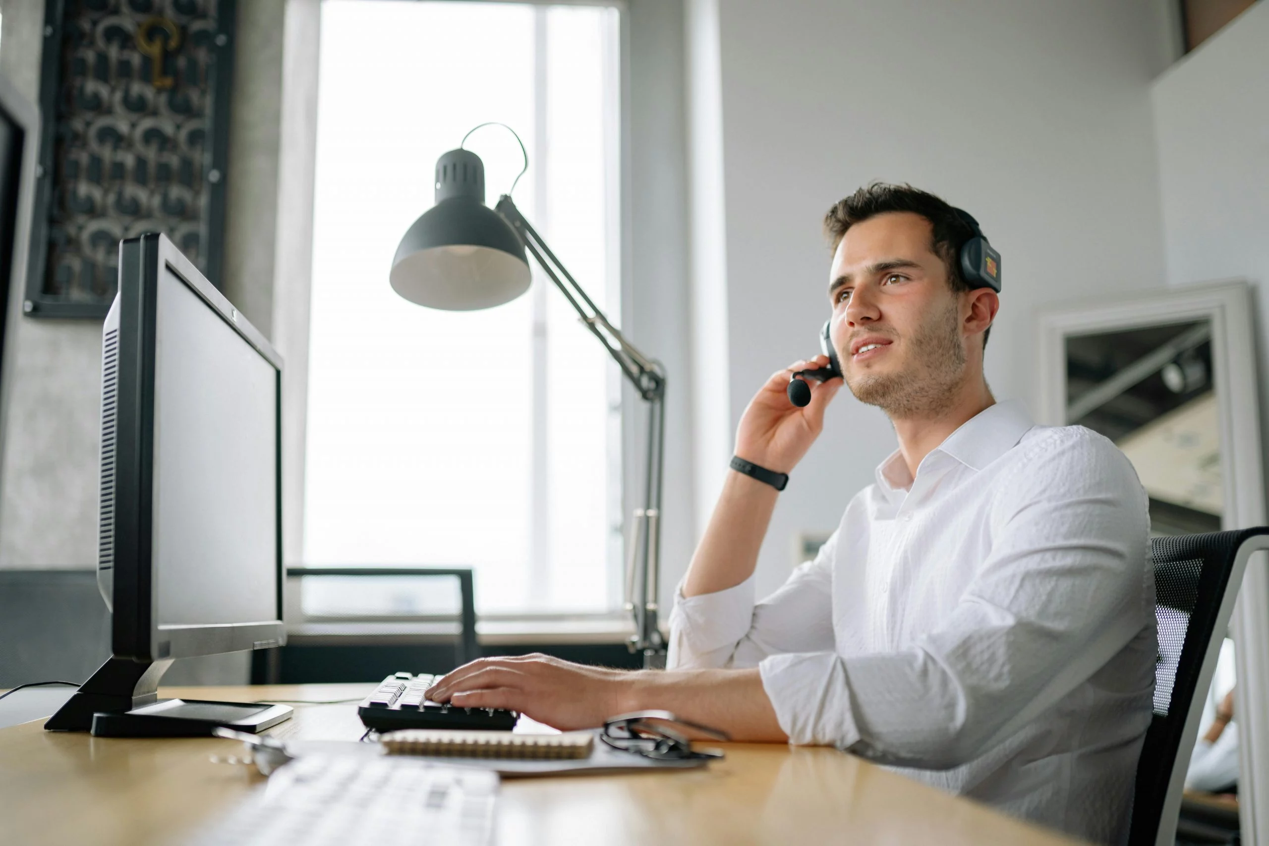 Mitarbeiter mit Headset arbeitet am Computer in einem hellen Büro und steht für persönliche Betreuung und direkte Unterstützung.