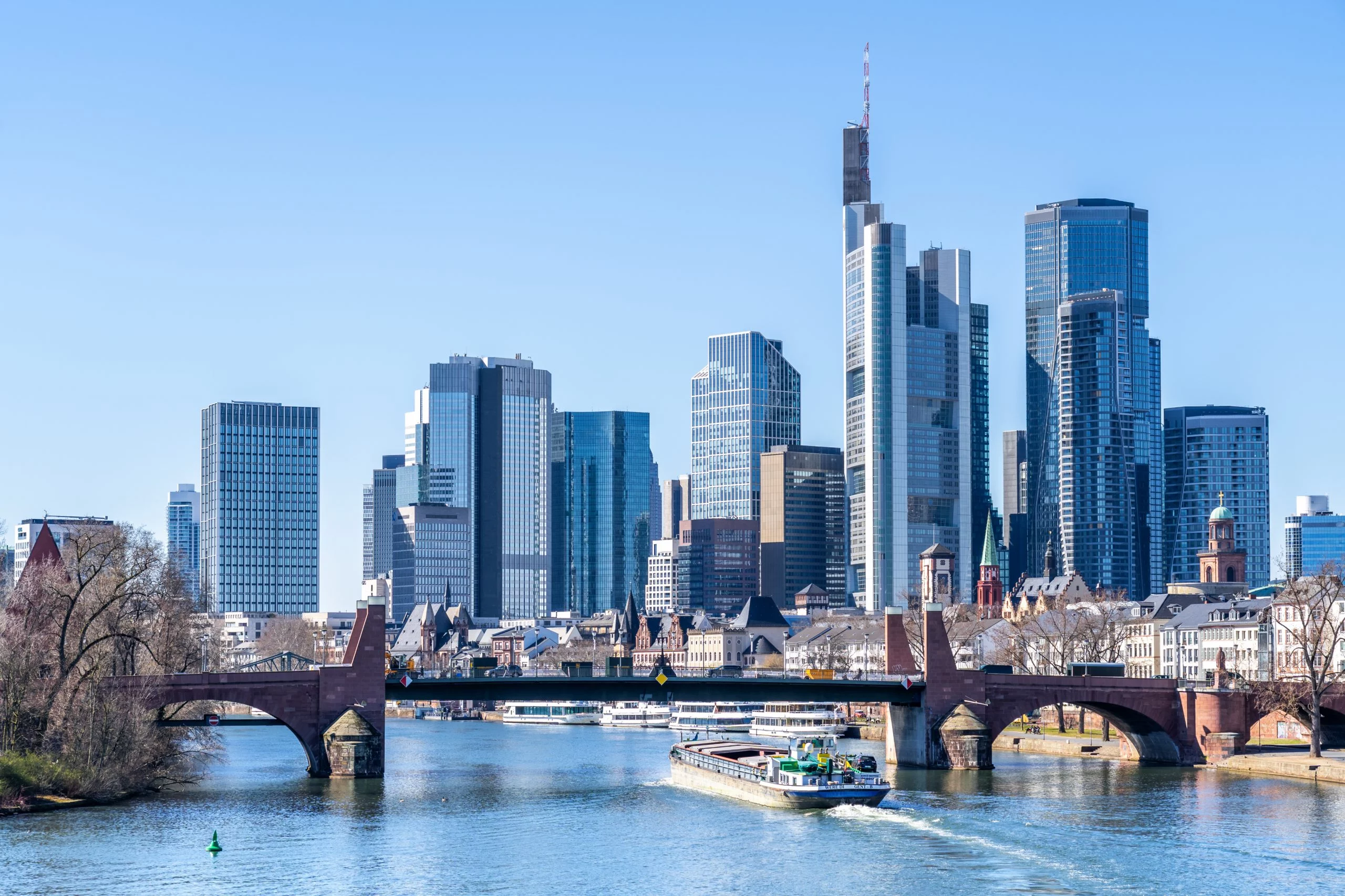 Blick auf die Frankfurter Skyline mit Main und Brücke bei sonnigem Wetter.